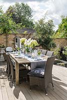 Dining table dressed for alfresco dining, on wooden deck in courtyard