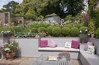 Sunken seating area in cottage garden with bench built in to retaining wall and fire-pit in metal table, Cheshire