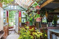 Old fashioned garden room, or potting shed, filled with vintage gardening equipment and paraphanalia, recycled stained glass victorian doors and windows