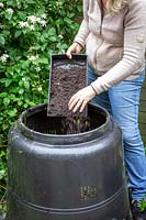 Mixing grass clippings with soil when adding to a compost bin.