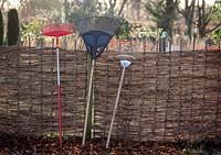 Different types of rakes leaning against a fence