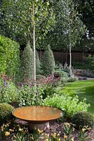Rust effect water bowl in garden with white stemmed birch trees, Pittosporum tenuifolium 'Silver Queen', Astrantias, Sedums and Agastache - July, Cheshire