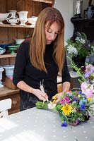 Zelie in the flower studio making hand tied bunches of flowers and securing with raffia.