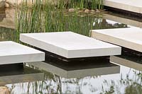 Floating stone stepping stones over a pond water feature, planted with Equisetum hyemale. A Japanese Reflection garden, RHS Malvern Spring Festival, 2016. Design: Peter Dowle and Richard Jasper - Howle Hill Nursery