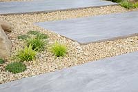 Large stone paving slab stepping stones with gravel bed planted with Carex morrowii. Cactus Direct Garden at RHS Tatton Park Flower Show, 2017. Designers: Michael McGarr at Warnes McGarr and Co.