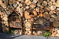 Wildlife friendly garden with a wall made from logs with insect hotels habitat for pollinators made with old bricks, twigs, tiles, cardboard, straw, dead grass, hollowed bamboo canes, pine cones and tree bark with alpine strawberry plants. The Family Garden. RHS Hampton Court Flower Show July 2018 - Designer: Lilly Gomm - Sponsors Practicality Brown, Marshalls, The Tree Company 