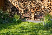 Wildlife and child friendly garden with a wall made from logs habitat for pollinators with insect hotels and an unmown long grass lawn. The Family Garden. RHS Hampton Court Flower Show July 2018  - Designer: Lilly Gomm - Sponsors Practicality Brown, Marshalls, The Tree Company 