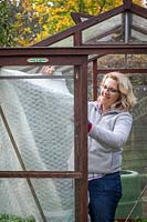 PInning up plastic bubblewrap to insulate a greenhouse ready for winter