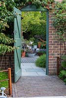 The entrance to a contemporary walled cottage garden with deck, seating and containers.