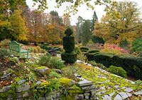 A moss covered stone terrace with a view over cloud shaped Taxus baccata and Buxus and autumn foliage on Quercus at the Arts and Crafts garden, High Moss, Portinscale, Cumbria, UK