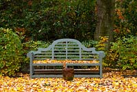 A Lutyens style garden bench surrounded by fallen autumn leaves in the garden at High Moss, Portinscale, Cumbria, UK