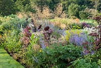 Rusty metal flower sculptures rest in a border of Russian sage, tobacco plants, purple angelica and Stipa gigantea.