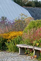 Rustic oak bench in front of perennial flower bed with converted old farm buildings behind