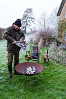 Man lighting a corten steel fire pit with rolled up newspaper on a frosty winter day. 