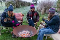 Women and dog sitting around a fire in a corten steel fire pit, keeping warm on a frosty winter day.