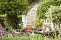 Architect's garden studio with outdoor seating area framed by standard hollies, box hedging and clipped ivy in a cottage garden in June. 