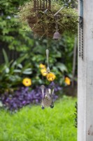 A handmade windchime made from repurposed forks and spoons and blue glass marbles suspended from a hanging basket in a backyard.