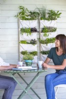 Woman sitting at a table next to hanging herb and salad garden