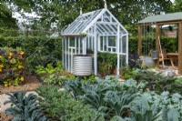 RHS No Dig Allotment Demonstration Garden. A greenhouse filled with chilli plants rests beside a bed of salad leaves, and overlooking rows of brassicas.