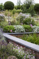 Retaining wall with slate top surrounded by lush planting in July.