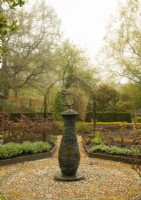 A stone sculpture surrounded by circular stone paving and raised beds in the kitchen garden at High Moss