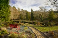 A bench painted Chinese red overlooking topiary hedge and lawn at High Moss