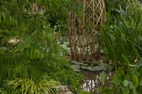 A laminated bamboo grid structure surrounded by a pool filled with aquatic plants in the Guangzhou China: Guangzhou Garden, winner of the Best Show Garden award at the RHS Chelsea Flower Show 2021