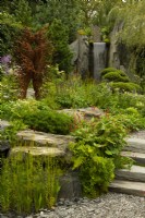 60 Degrees East, a garden between continents, a figurative metal sculpture beside a waterfall on a hillside surrounded by European and Asian planting.  Sculptures by Penny Hardy