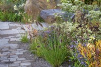 The M and G Garden. Paved area with a mix of gravel and paving for improved drainage, and rock and carved wooden bench. Autumn planting combination including Sesleria autumnalis, Eurybia x herveyii, Aster umbellatus, Selinum wallichianum, Pennisetum alopecuroides 'Cassian' and autumn tints of Amsonia illustris.