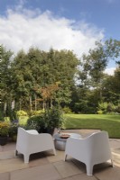 Stone patio area with metal table and modern chairs looking out onto garden - Cheshire - July