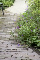 Curvy path of bricks with Geranium in mixed flower border.