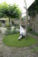 Curvy path of bricks with round shaped lawn and woman sitting and reading in the hammock.