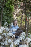 Women siting in the garden with dogs on her lap. She is surrounded by Amelanchier 'lamarckii', Trachelospermum jasminoides, Photinias and a beech hedge, Fagus sylvatica.