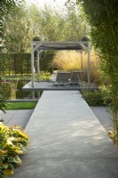 Path leading to lounge chairs on terrace, pergola with Molina arundinacea.