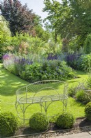 View of garden in summer with herbaceous borders. Wirework garden seat, box topiary balls June
