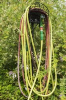 Wound professional grade yellow and red rubber garden watering hoses with green water spray gun attached, Quebec, Canada - July