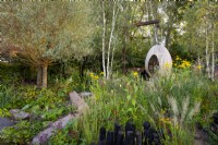 Egg shape swing seat surrounded by Kniphofia 'Tawny King', Rudbeckia laciniata 'Herbstonne', Calamagrostis acutiflora 'Karl Foerster', Calamagrostis brachytricha and Salix Alba. The Yeo Valley Organic Garden. Designer: Tom Massey, supported by Sarah Mead, Chelsea Flower Show 2021. 