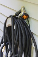 Back stretch watering hose with attached water spray gun wound on holder mounted on exterior wall of house - August