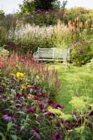 Metal bench surrounded by borders packed with herbaceous perennials  at Highfield Farm in August.