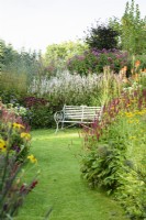 Metal bench surrounded by borders packed with herbaceous perennials including persicarias, echinaceas and eupatoriums at Highfield Farm in August.