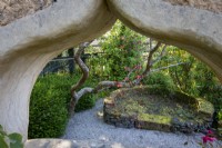 Cob wall structure in garden, with arched window 'peephole' through to secret garden