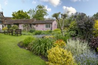 Pink outbuildings behind a colourful mixed border at Mill Street Gardens - May