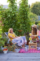 Women relaxing on roof terrace, container plants include tomatoes, herbs and flowers.