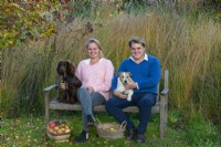 Couple sitting on bench with pet dogs after harvesting apples.