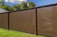 Brown chain-link fence with privacy slats in residential backyard - September