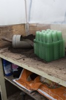 A potting bench in a small commercial nursery with wooden handled scoop, compost and a bulk lot of seed trays in the foreground and a bag of compost underneath. Spring. 