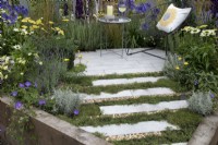 'The Power of Flowers is Everything' at BBC Gardener's World Live 2021 - camomile interspered with slim paving slabs and gravel leading to contemporary seating area surrounded by yellow and blue perennials