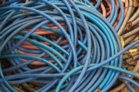 Coiled blue, orange and grey rubber heavy duty garden hoses on the ground in autumn - October
