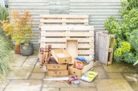 Pallets, drawers, spindles, jigsaw, drill, black paint, brush, roller, screws, saw, tape measure and pencil laid out on the ground