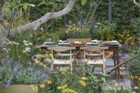 Sheltered garden full of fragrant plants and edible herbs. Patio overhung by a Ficus carica fig tree with wooden table and chairs set for a meal and centrepiece cut flower posy in wooden box 

The Parsley Box Garden

Designer: Landform Consultants Alan Williams

RHS Chelsea Flower Show 2021